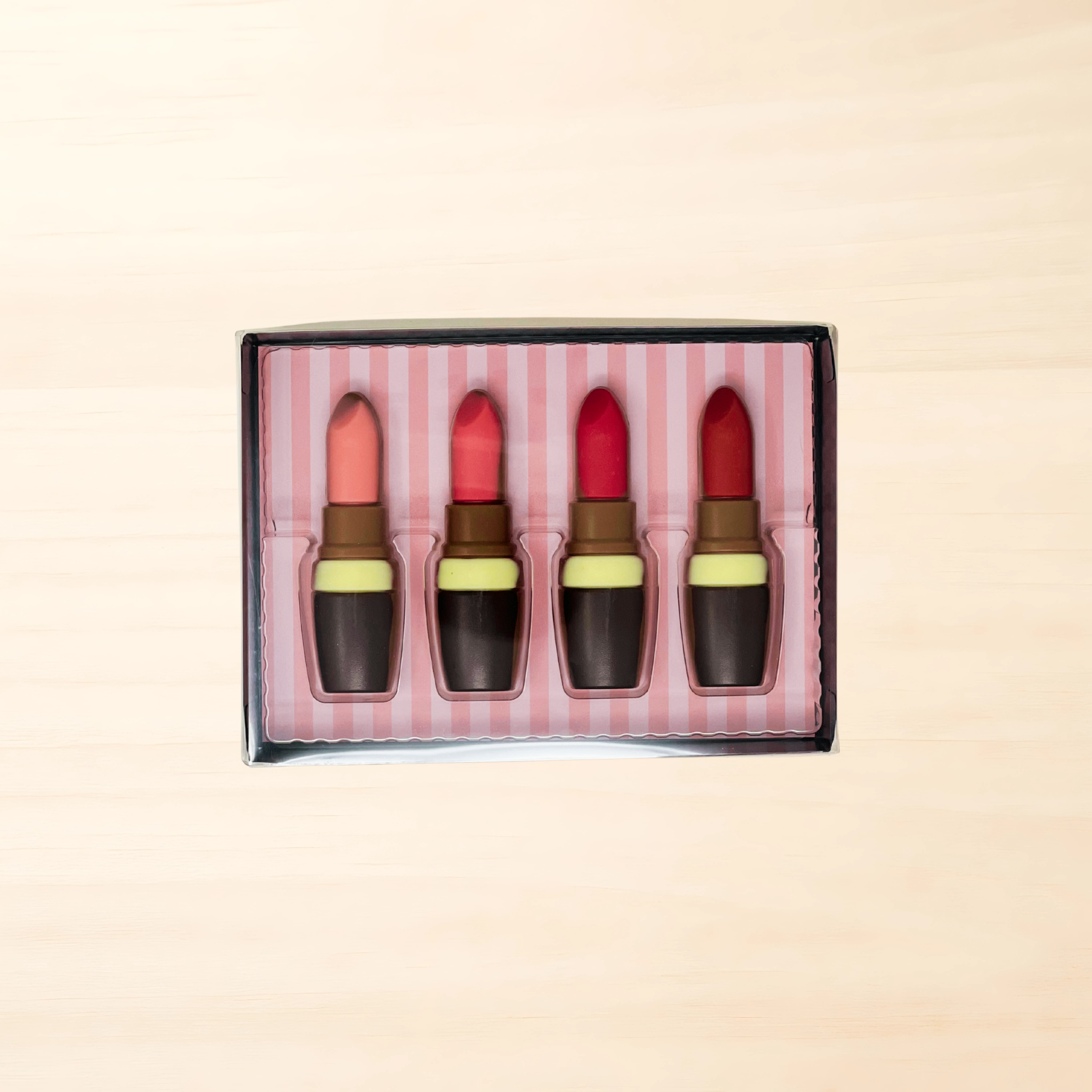 Schokoladen-Lippenstifte in rosa, rot, dunkelbraun und hellbraun in einer Geschenkverpackung.