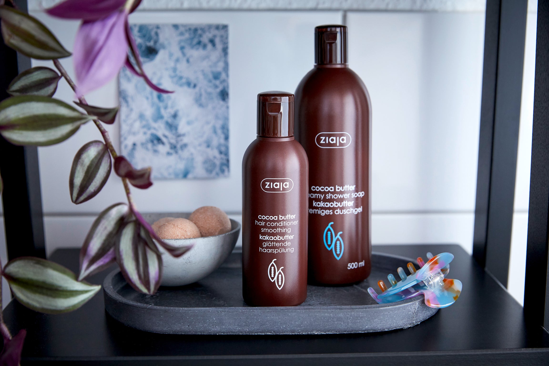 Badregal mit Pflegeprodukten, u.a. sieht man auf einem schwarzen Tablett eine chüssel mit Badekugeln und zwei Flaschen der Marke Ziaja. Die Flaschen sind braun mit weißer Schrift.