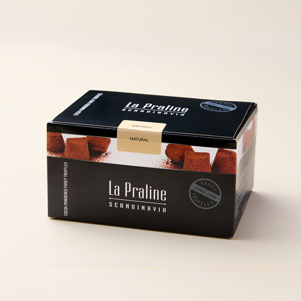 Schwarze Papp-Box mit weißer Aufschrift und weißer Banderole mit braunen Pralinen