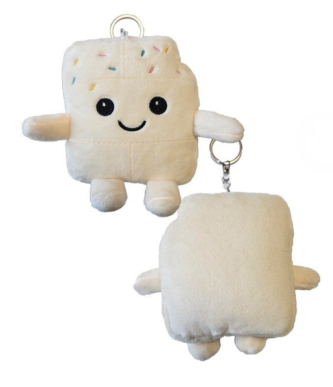 Weißer Plüsch-Schlüsselanhänger in Form einer Schokoladentafel mit bunten Streuseln und lächelndem Gesicht, liegend auf einer Holzoberfläche.