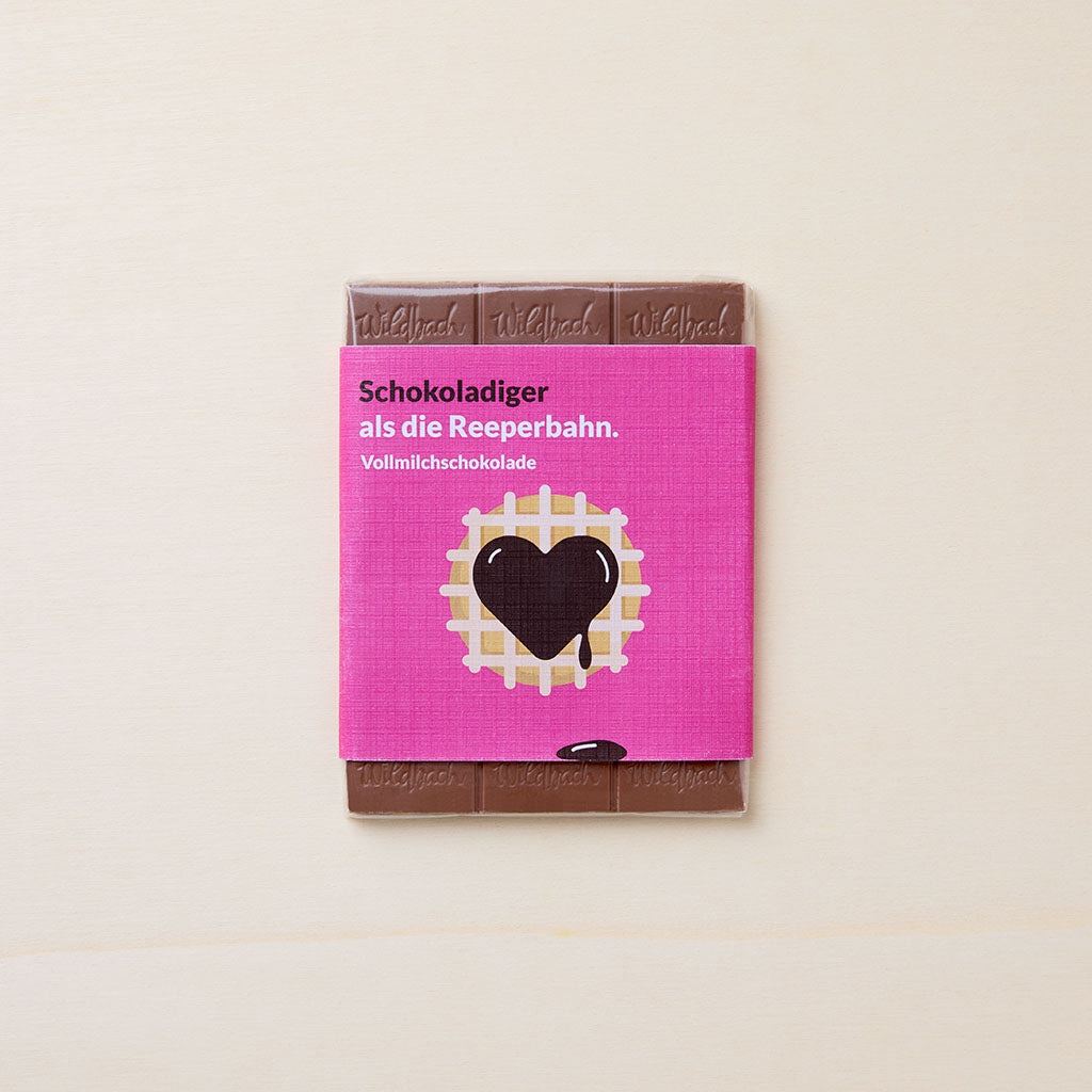 Vollmilchschokolade in pinkem Wickler mit der Abbildung einer grafischen Waffel mit einem herzförmigen Schokoklecks und Artikelbezeichnung in weißer und dunkelbrauner Schriftfarbe