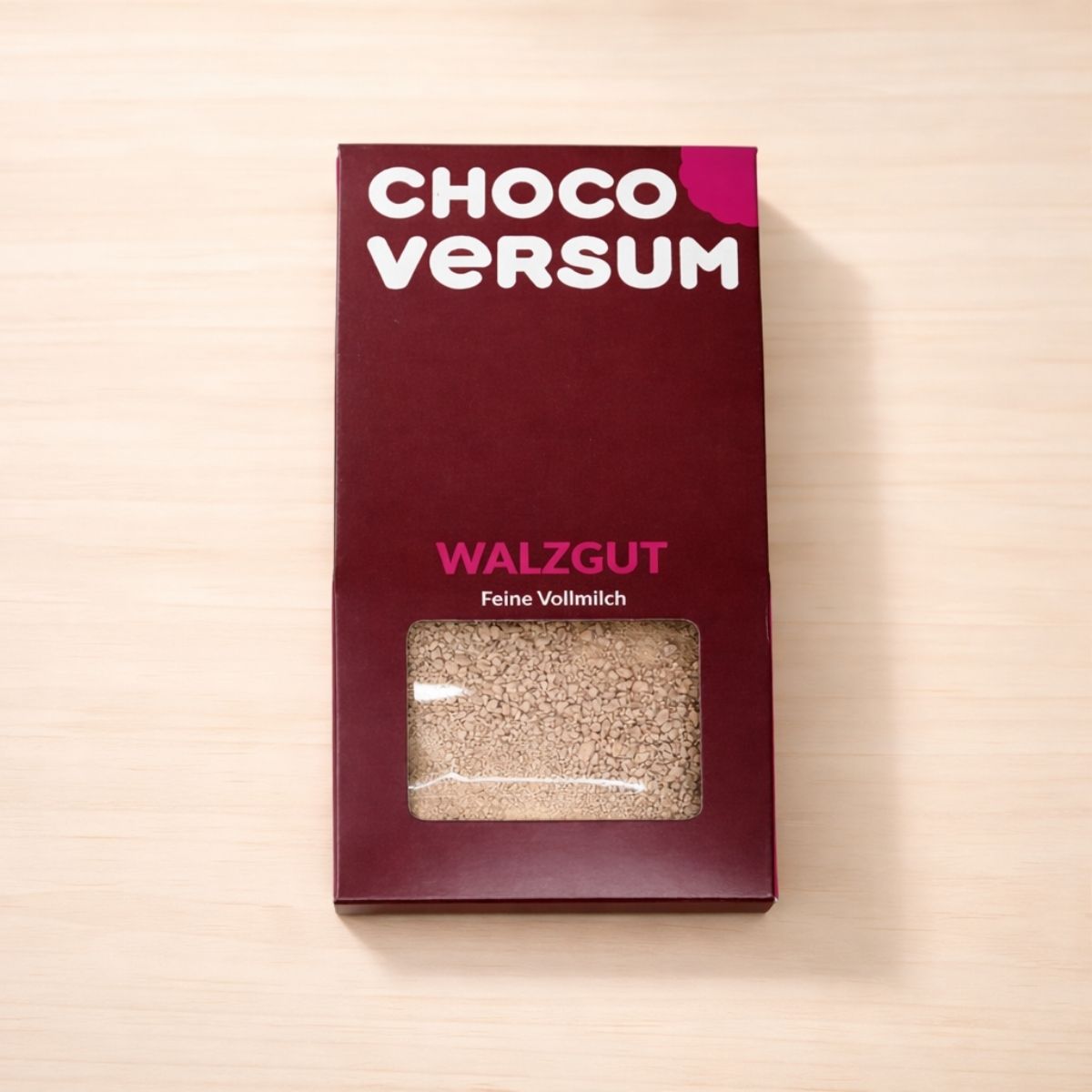 CHOCOVERSUM Walzgut Feine Vollmilch in schokoladenfarbener Verpackung mit pinken Hervorhebungen und Sichtfenster, das feine geraspelte Vollmilchschokolade zeigt.