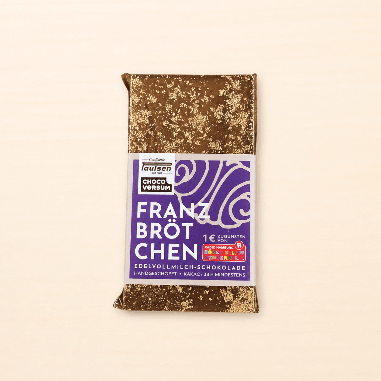Handgeschöpfte Edelvollmilch-Schokolade „Franzbrötchen“ von Confiserie Paulsen mit violetter Banderole und goldgesprenkelter Schokoladenoberfläche.