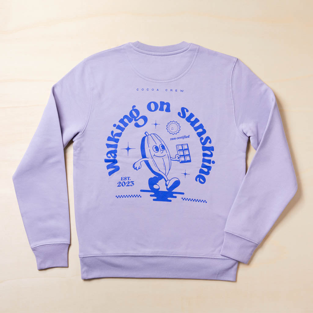 fliederfarbener Sweater Rückseite mit lila Aufdruck Cocoa Crew & "Walking on Sunshine" mit wandernder Kakaofrucht im Comicstyle