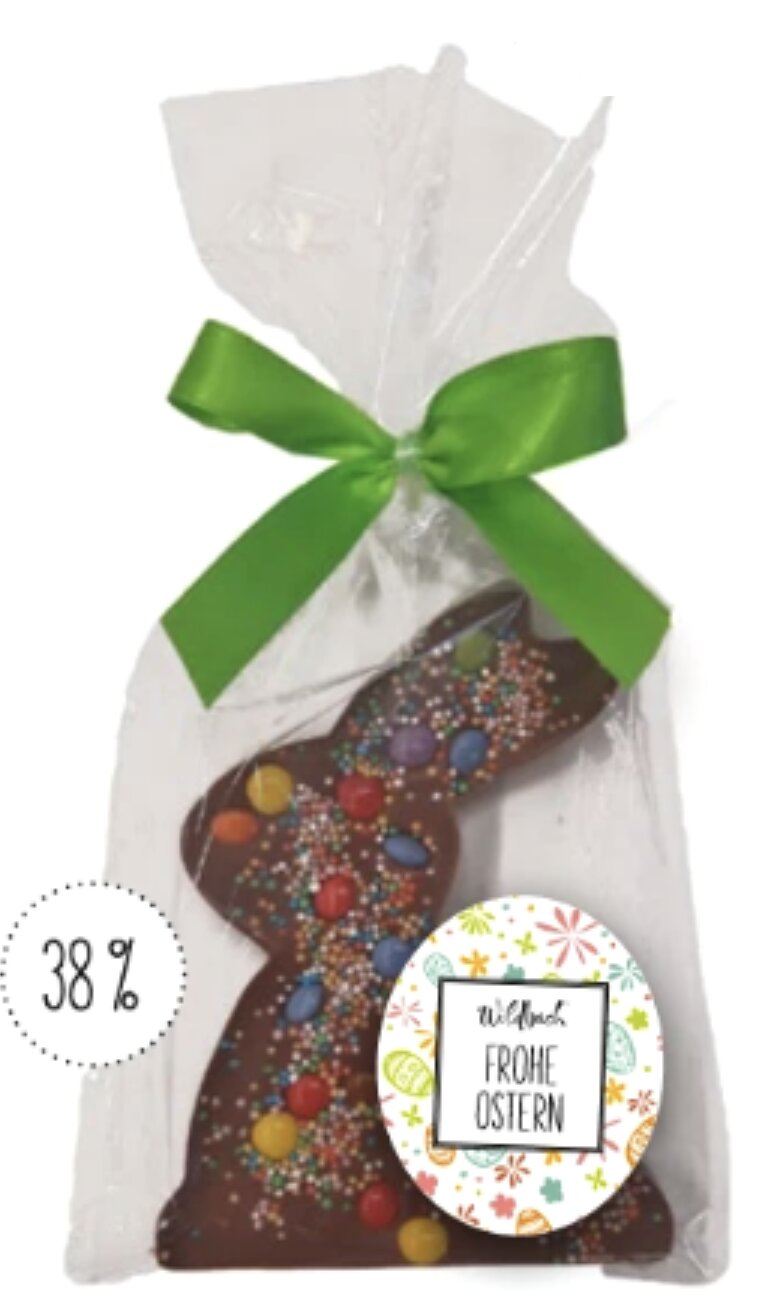 Vollmilch-Schokoladenhase mit bunten Schokolinsen und Zuckerstreuseln, verpackt in transparenter Folie mit grüner Schleife.