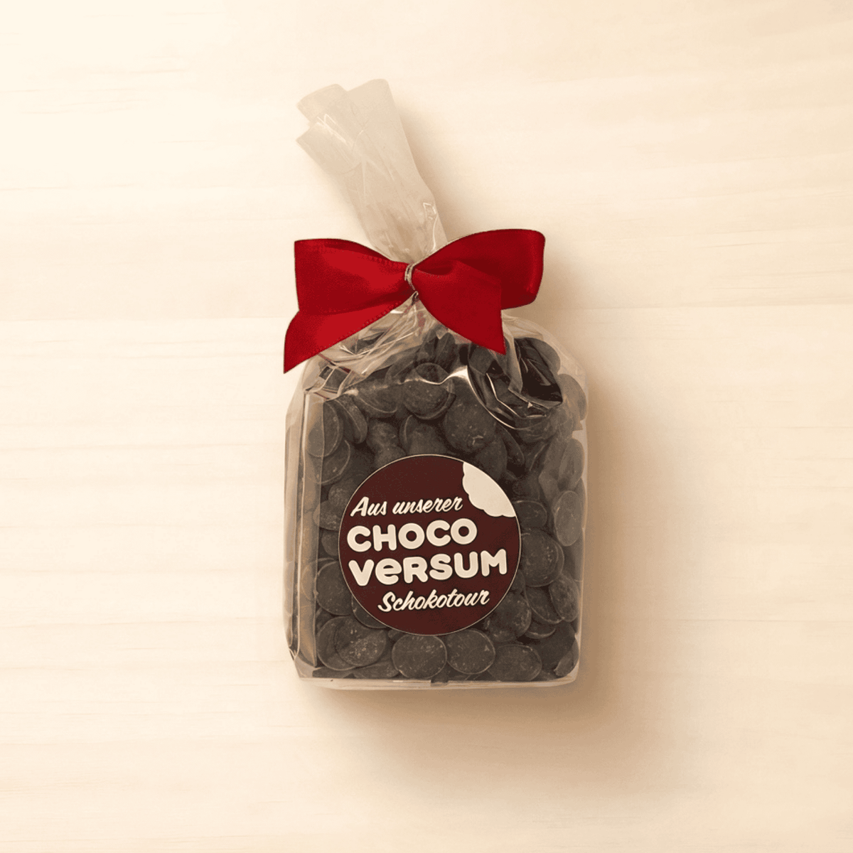CHOCOVERSUM Zartbitter-Kuvertüre Ghana mit 60 % Kakao im 140-g-Beutel mit roter Schleife.