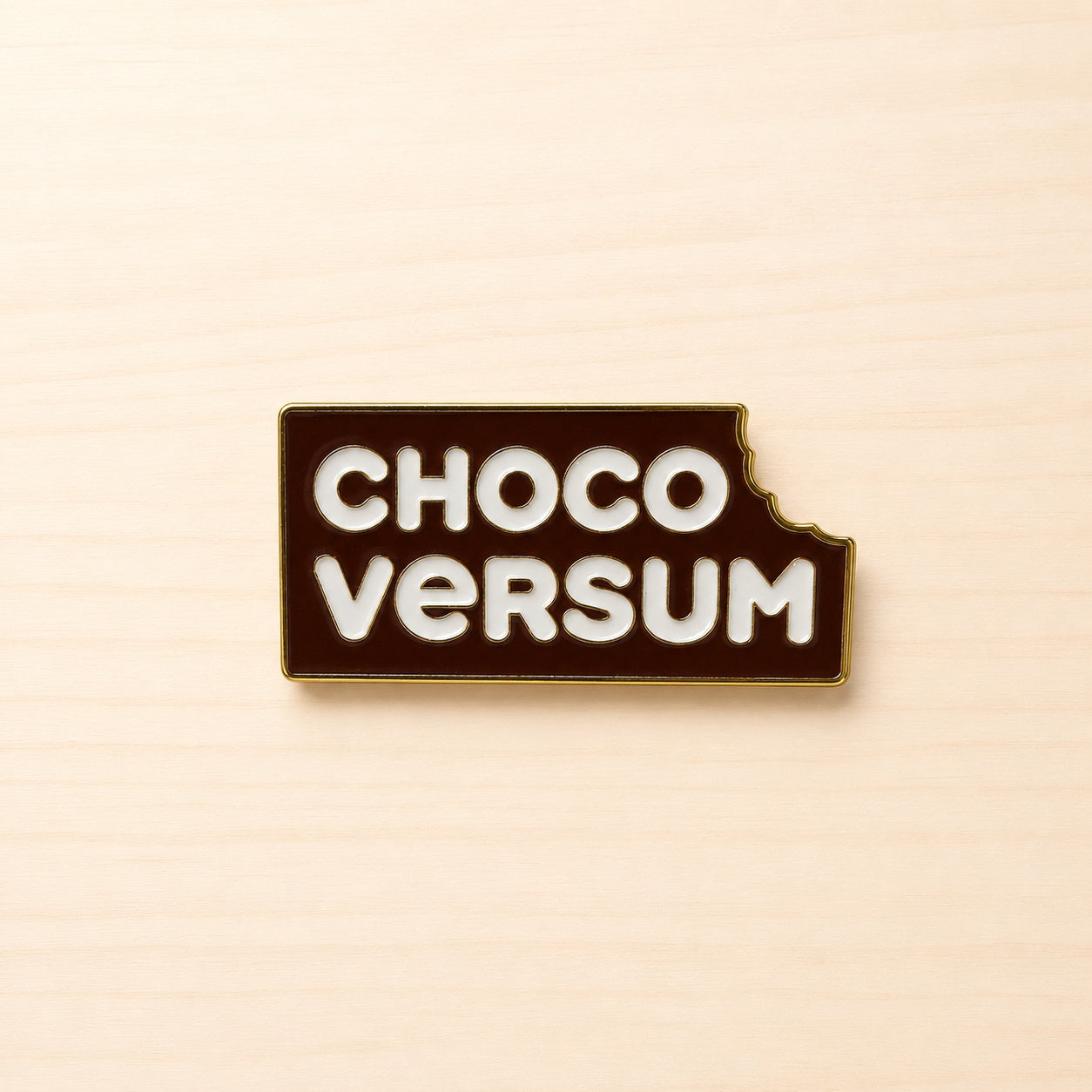 Metall-Ansteck-Pin mit braunem CHOCOVERSUM Logo, heller Schrift, goldfarbener Umrandung und angebissener Ecke.
