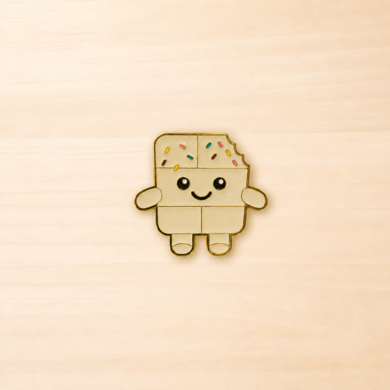 Metall-Ansteck-Pin „Sprinkles“ in Form einer lächelnden weißen Schokoladenfigur mit bunten Streuseln und goldfarbener Umrandung.