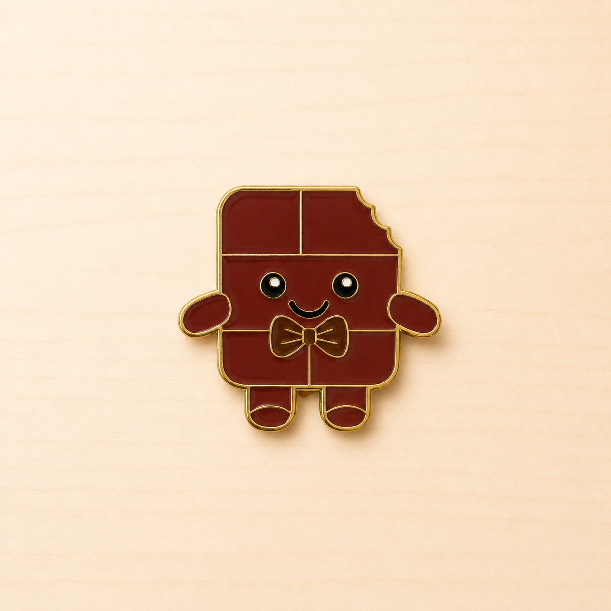 Metall-Ansteck-Pin „Chocolino“ als lächelnde braune Schokoladenfigur mit Fliege und goldfarbener Umrandung.