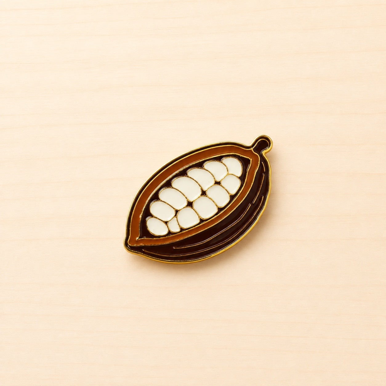 Metall-Ansteck-Pin in Form einer geöffneten braun-orangefarbenen Kakaofrucht mit hellen Kakaosamen und goldfarbenen Konturen.
