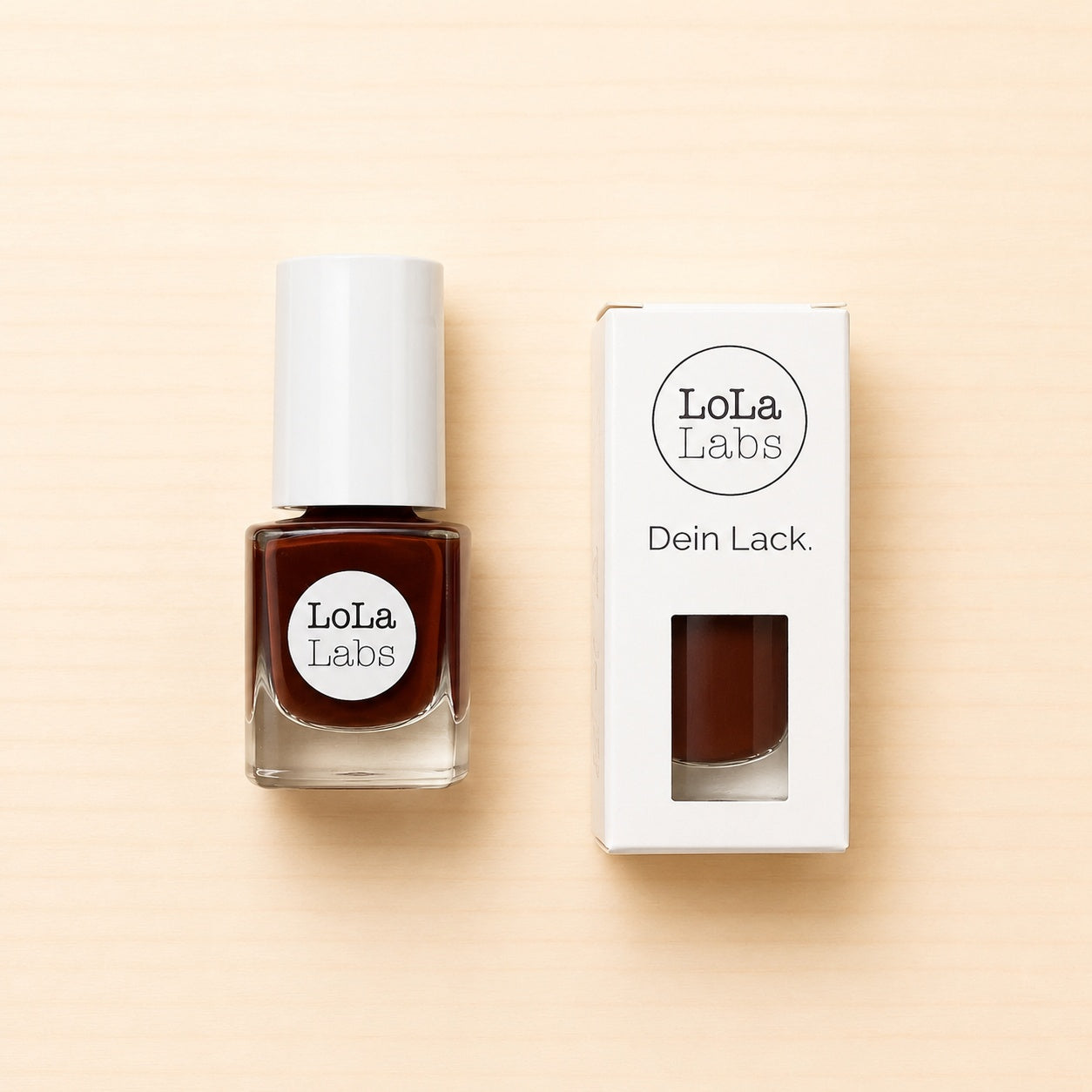 LoLaLabs Nagellack „Vollmilch“ in einem 5-ml-Glasfläschchen mit weißem Verschluss neben der weißen Produktverpackung. Der warme schokoladenbraune Farbton ist durch das Sichtfenster der Verpackung erkennbar.