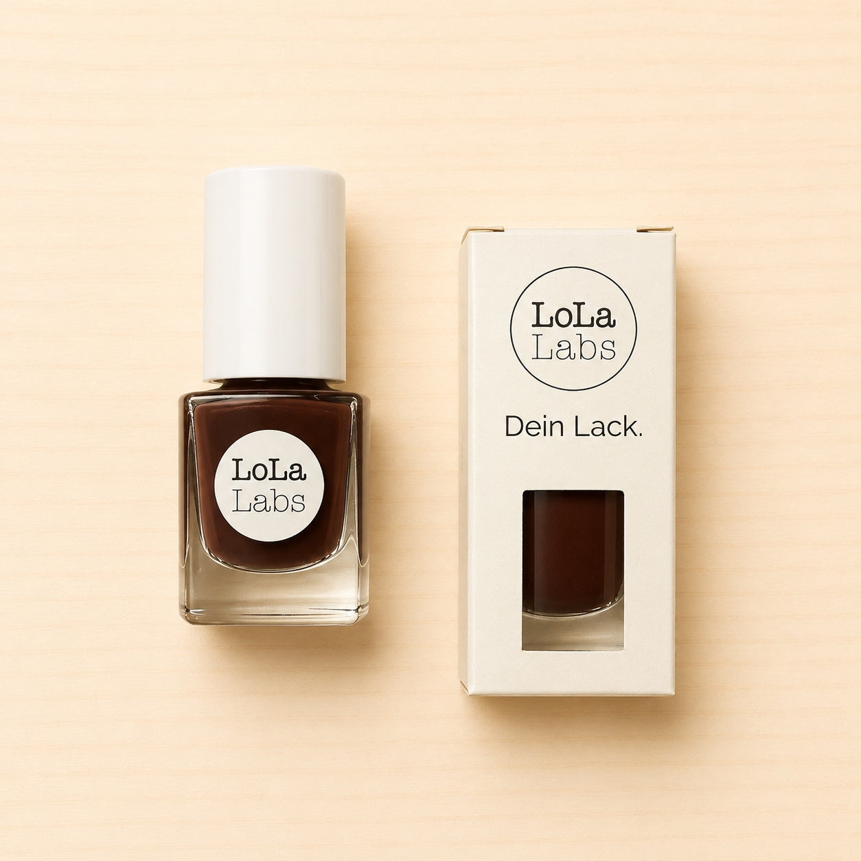 LoLaLabs Nagellack „Zartbitter“ in einem 5-ml-Glasfläschchen mit weißem Verschluss neben der weißen Produktverpackung. Der dunkle schokoladenbraune Farbton ist durch das Sichtfenster der Verpackung erkennbar.
