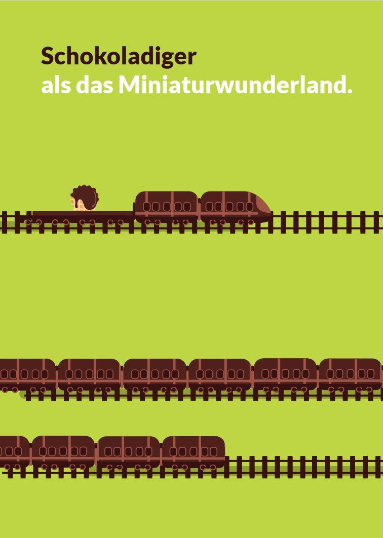 Grüne Postkartenvorderseite mit Eisenbahn in Schokoladenoptik im Vordergrund und darüber Aufschrift "Schokoladiger als das Miniaturwunderland" in dunkelbraunen und weißen Lettern