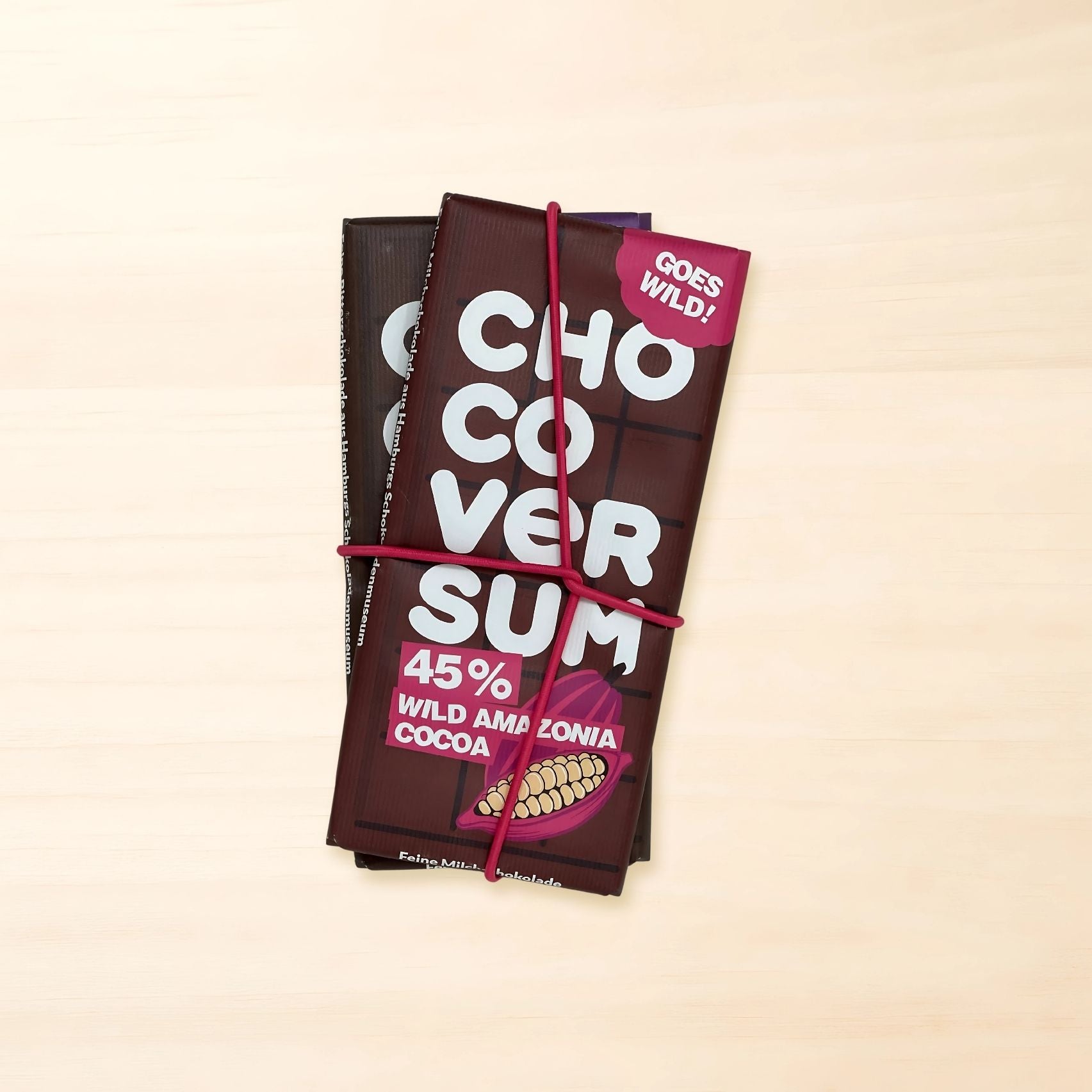 Zwei CHOCOVERSUM Wild Amazonia Schokoladentafeln – 45 % Vollmilch- und 72 % Bitterschokolade – als Bundle mit pinkem Gummiband zusammengehalten.