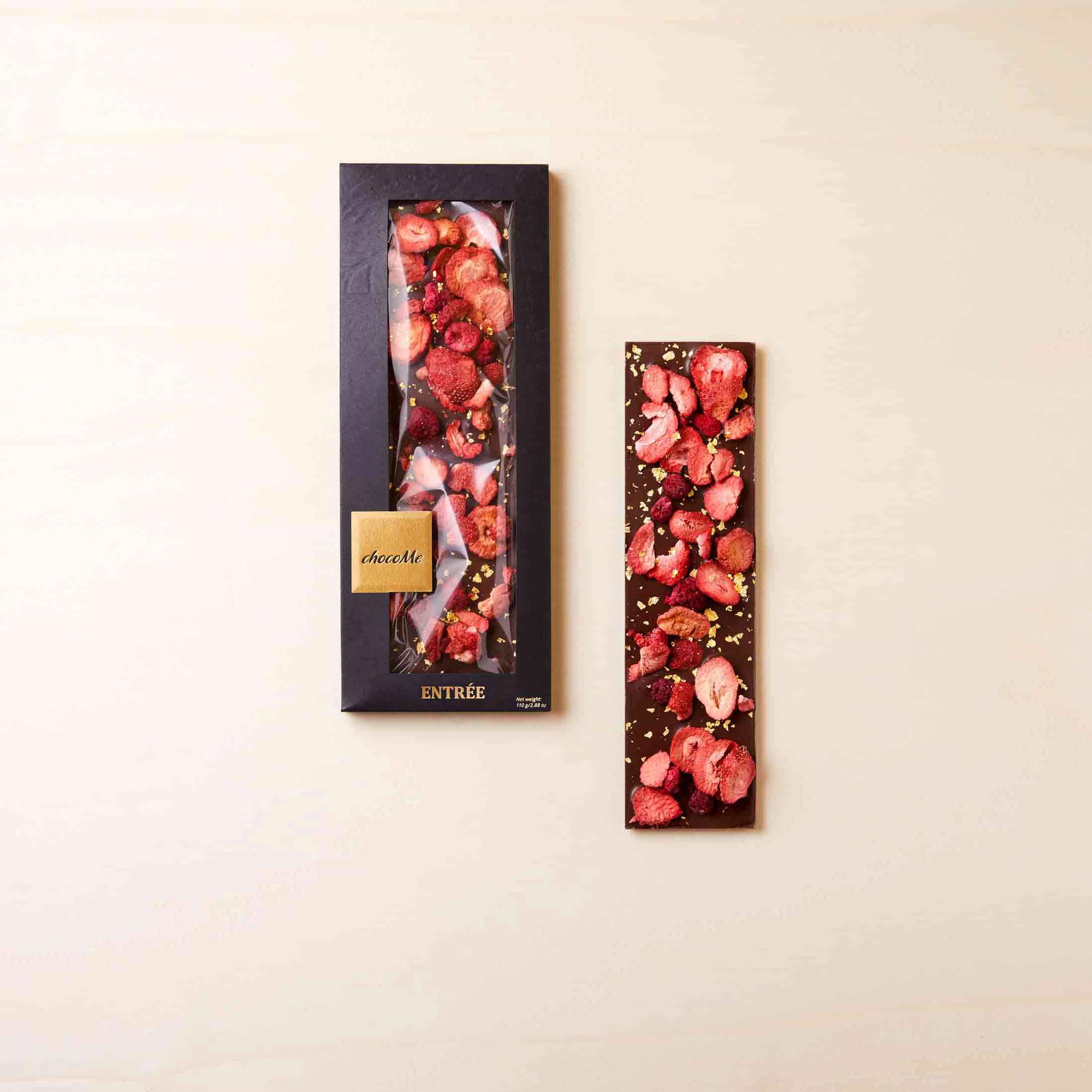 Schokoladentafel mit Erdbeeren, Himbeeren und essbaren Gold, eine Tafel in der dunklen Verpackung und eine ausgepackte Tafel liegt daneben.