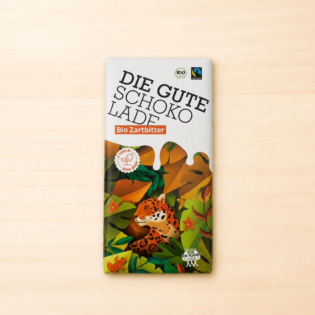 Verpackung der Schokoladentafel „Die Gute Schokolade – Bio Zartbitter“ mit weißem oberen Bereich, farbenfroher Dschungelillustration mit Jaguar im unteren Teil sowie BIO-, Fairtrade- und Plant-for-the-Planet-Logos. 