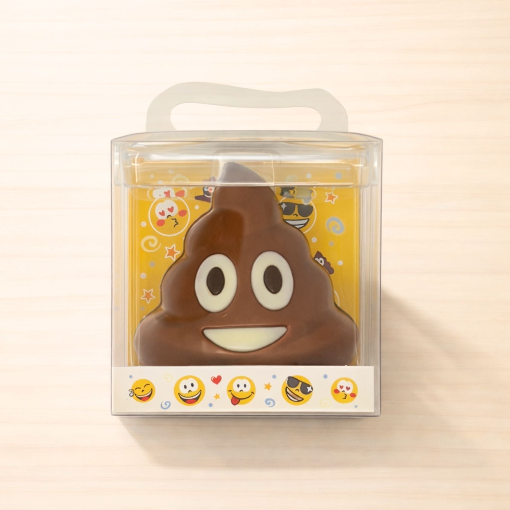 Lustige Schokoladenfigur aus Vollmilchschokolade in Form eines Kackhaufen-Emojis, verpackt in transparenter Geschenkbox mit buntem Emoji-Design